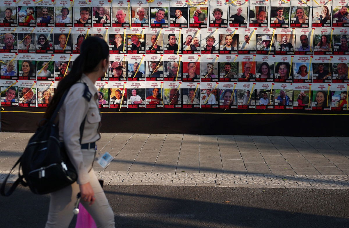 <i>Florion Goga/Reuters via CNN Newsource</i><br/>A woman walks next to a wall of posters of hostages kidnapped during the deadly October 7 attack on Israel by Hamas