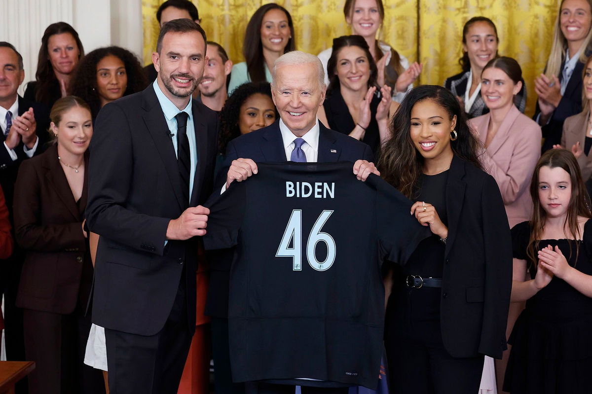 <i>Kevin Dietsch/Getty Images via CNN Newsource</i><br/>President Joe Biden is presented a jersey from NJ/NY Gotham FC head coach Juan Carlos Amorós and forward Midge Purce during a ceremony.