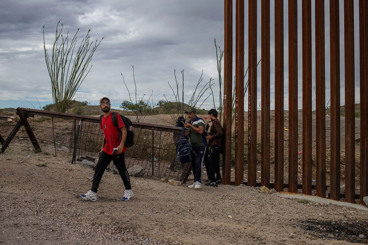 <i>Adrees Latif/REUTERS/REUTERS via CNN Newsource</i><br/>A smuggler stands in the background as asylum-seeking migrants from India cross the Border Wall into the United States from Mexico