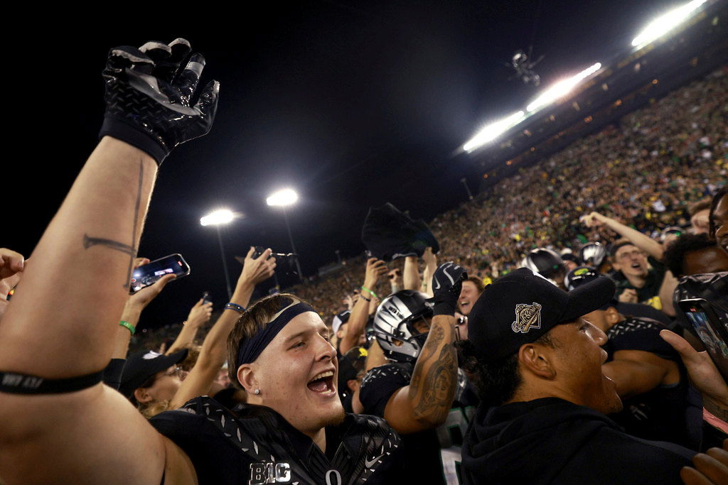 Oregon tight end Kade Caton, left, and fans celebrate on the field after winning an NCAA college football game against Ohio State, Saturday, Oct. 12, 2024, at Autzen Stadium in Eugene 