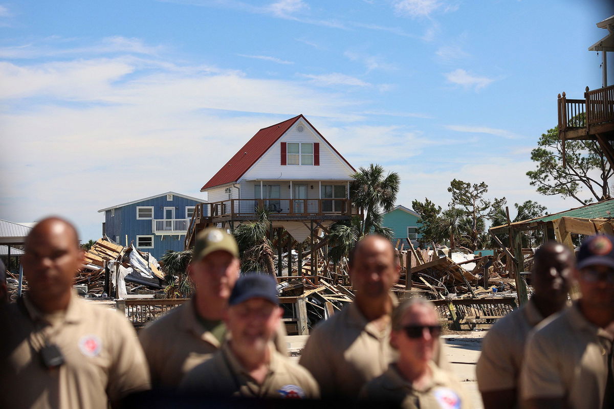 <i>Tom Brenner/Reuters via CNN Newsource</i><br/>First responders watch President Joe Biden's motorcade against the backdrop of damaged properties in Keaton Beach