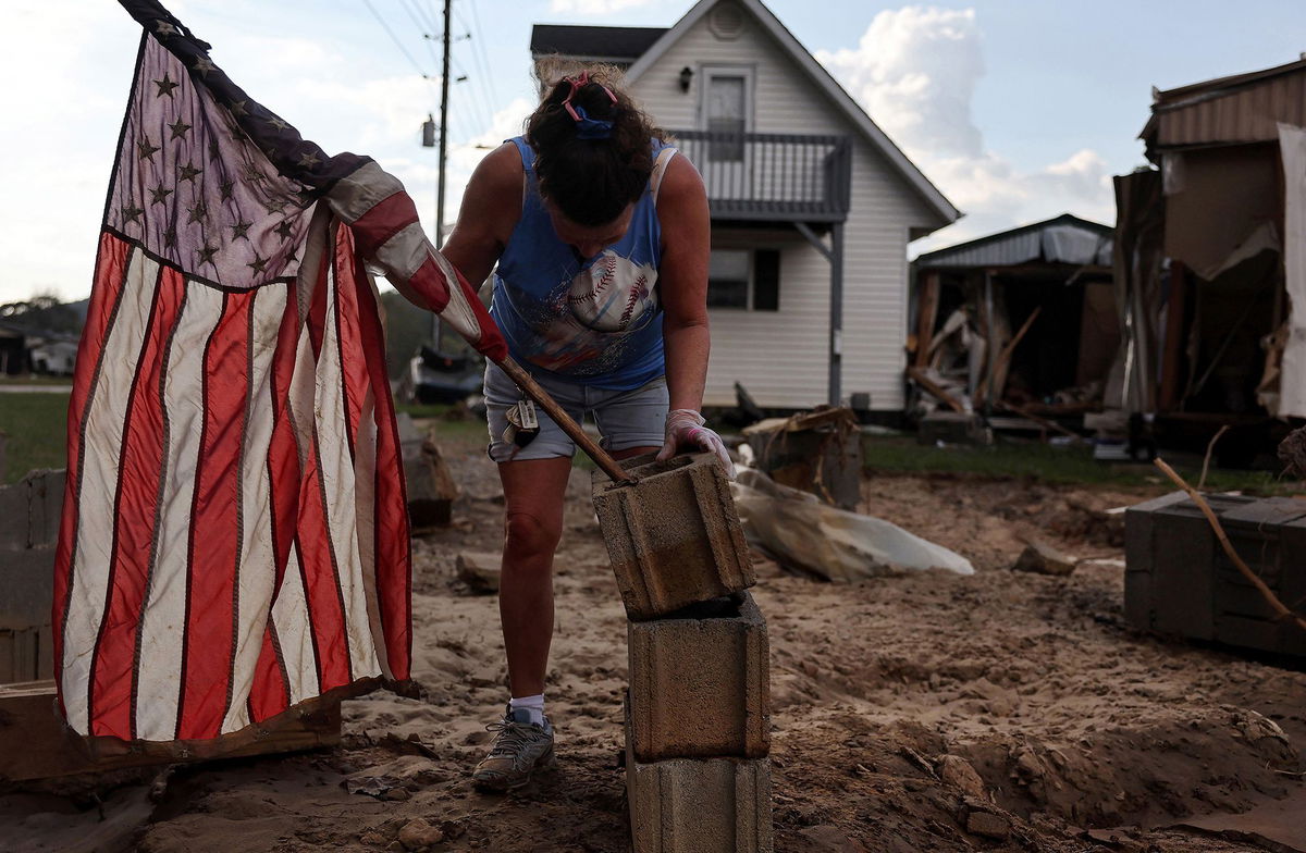 <i>Mario Tama/Getty Images via CNN Newsource</i><br/>Roxanne Brooks mounts an American flag to a stack of cinderblocks outside her friend's destroyed mobile home (R) in the aftermath of Hurricane Helene flooding on October 6 in Swannanoa