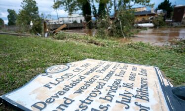 A sign commemorating the flood of 1916 lies on the ground next to a flooded waterway near Biltmore Village.