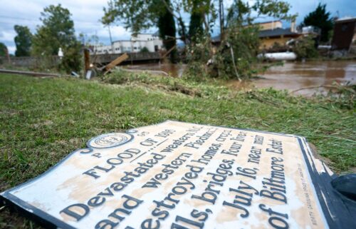 A sign commemorating the flood of 1916 lies on the ground next to a flooded waterway near Biltmore Village.