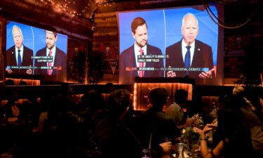 Sen. JD Vance and Gov. Tim Walz are shown on screen during a vice presidential debate watch party in New York on October 1.