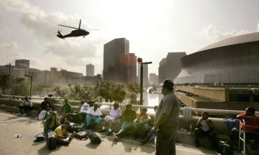 People seek high ground on Interstate 90 as a helicopter prepares to land at the Superdome in New Orleans in August 2005.