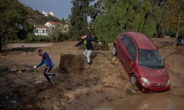 Men run next to a car covered with mud on a flooded street in Alora