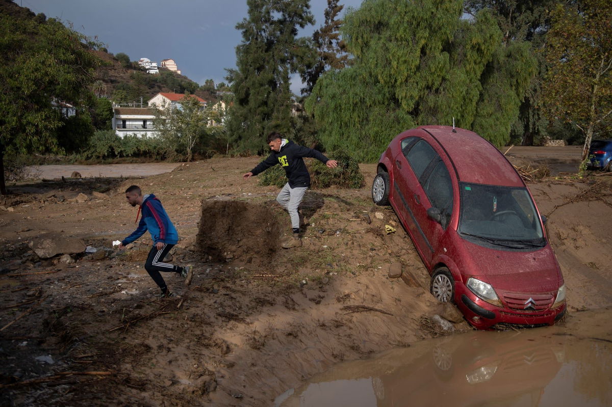 <i>Jorge Guerrero/AFP/Getty Images via CNN Newsource</i><br/>Men run next to a car covered with mud on a flooded street in Alora