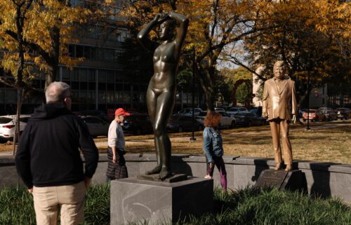 Pedestrians look at a statue of Donald Trump behind Gerhard Marcks' sculpture Maja