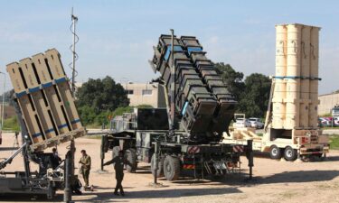 Israeli soldiers walk near an Israeli Iron Dome defense system (left)