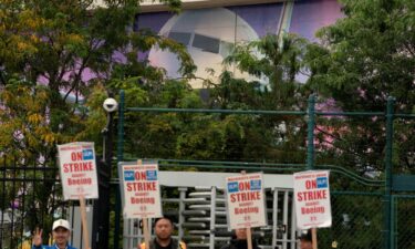 The image of a Boeing 737 jetliner is seen behind Boeing factory workers and supporters as they gather on a picket line during the third day of a strike near the entrance to a Boeing production facility in Renton