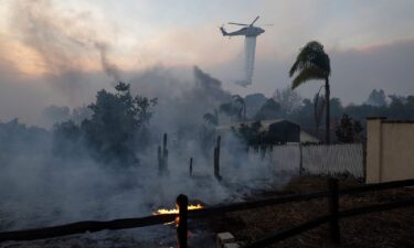 A helicopter drops water over a burning structure during a fast-moving wildfire in Moorpark