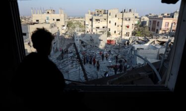 A Palestinian man looks out of a damaged window as he views the site of an Israeli strike on a house