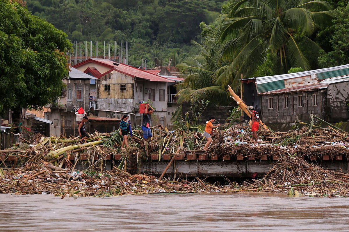 <i>Charism Sayat/AFP/Getty Images via CNN Newsource</i><br/>Residents cross a bridge filled with debris due to heavy rains brought about by Tropical Storm Trami in Polangui town