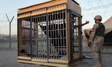 A detainee in an outdoor solitary confinement cell talks with a military police officer at the Abu Ghraib Prison in June 2004.