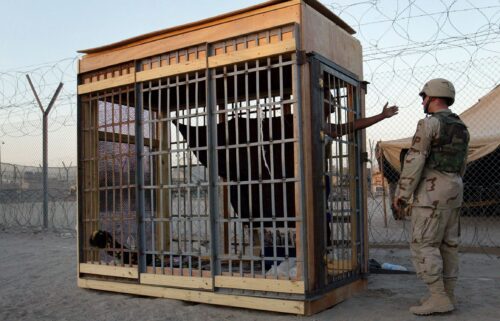 A detainee in an outdoor solitary confinement cell talks with a military police officer at the Abu Ghraib Prison in June 2004.