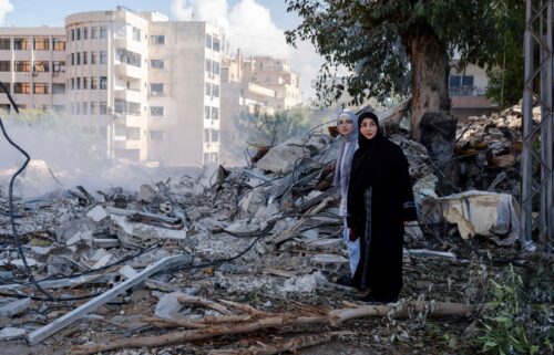 Two women stand next to destruction in the city center of Tyre