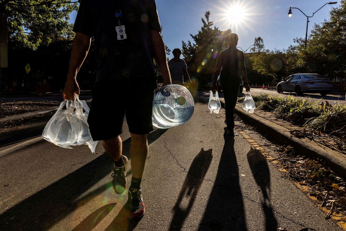 <i>Eduardo Munoz/Reuters via CNN Newsource</i><br/>People walk with water collected from a truck in Asheville