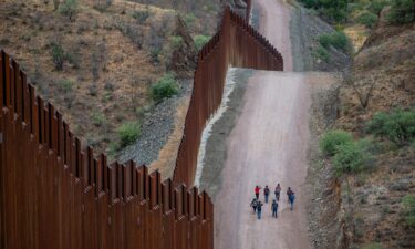 Migrants seeking asylum from Central and South America walk alongside border fencing in Ruby