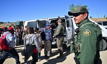 Customs and Border Patrol agents load migrants into a vehicle after groups of migrants walked into the US from Mexico at Jacumba Hot Springs