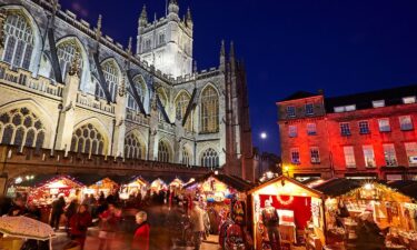 The Bath Christmas Market is illuminated at night behind Bath Abbey.