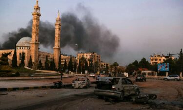 Smoke billows in the distance as damaged cars are seen at the site of Syrian regime airstrikes targeting opposition fighters in Aleppo