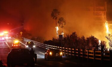 Firefighters work as the Franklin Fire burns near a building on Tuesday in Malibu