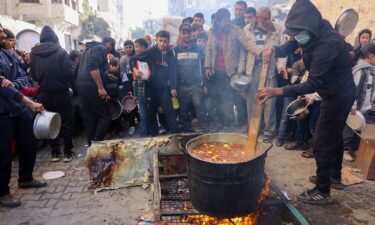 A volunteer stirs a food pot as Palestinians wait to collect humanitarian aid portions