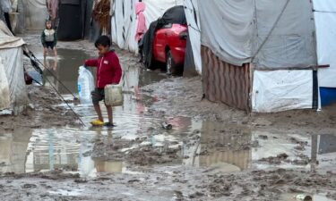 A boy walks down a flooded road in between makeshift tents in Deir Al-Balah