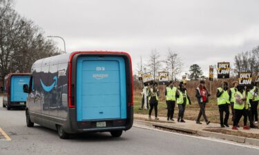 Amazon delivery trucks pass people holding signs and marching during a strike by Teamsters union members at an Amazon facility in Alpharetta