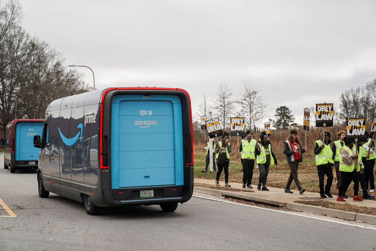 <i>Elijah Nouvelage/Reuters via CNN Newsource</i><br/>Amazon delivery trucks pass people holding signs and marching during a strike by Teamsters union members at an Amazon facility in Alpharetta