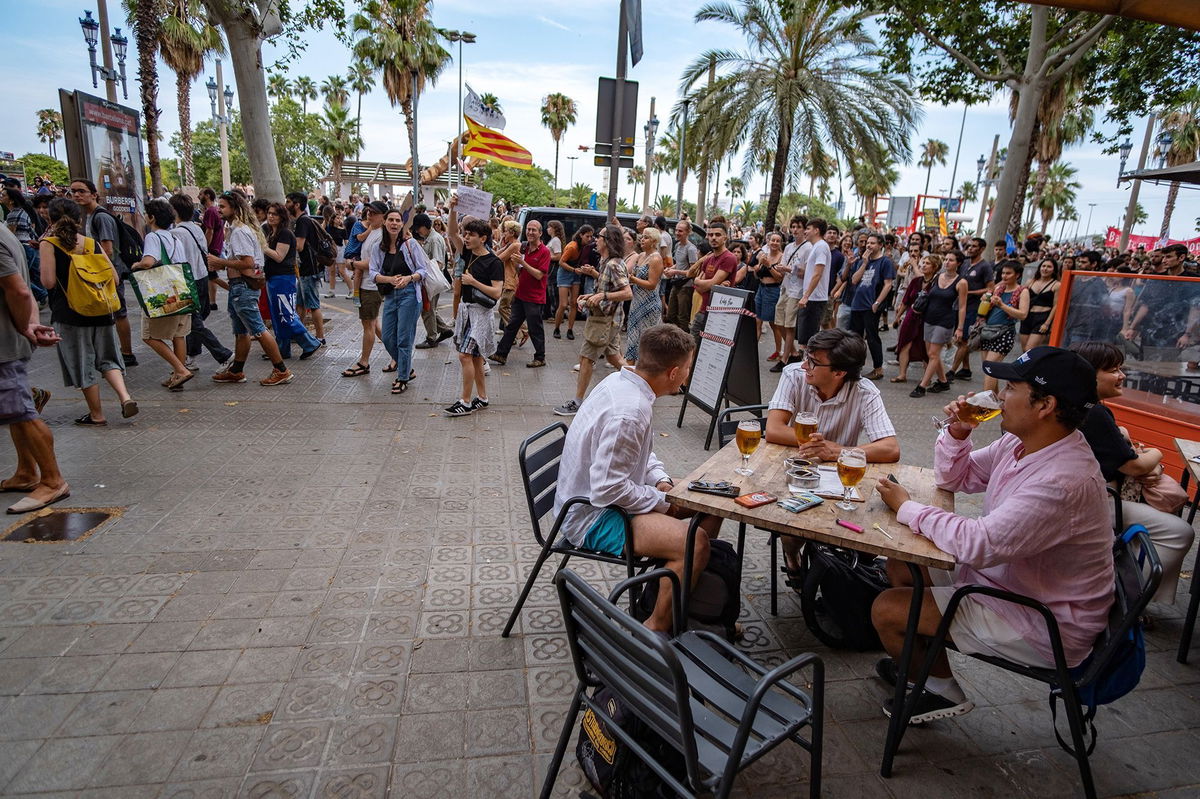 <i>Paco Freire/SOPA Images/LightRocket/Getty Images via CNN Newsource</i><br/>People drink beer outside a bar-restaurant while an anti-tourism demonstration passes by in Barcelona in July 2024.