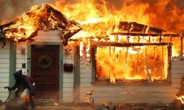 A resident uses a garden hose in an effort to save a neighboring home in Altadena