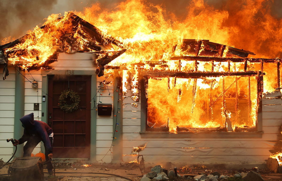 <i>Mario Tama/Getty Images via CNN Newsource</i><br/>A resident uses a garden hose in an effort to save a neighboring home in Altadena