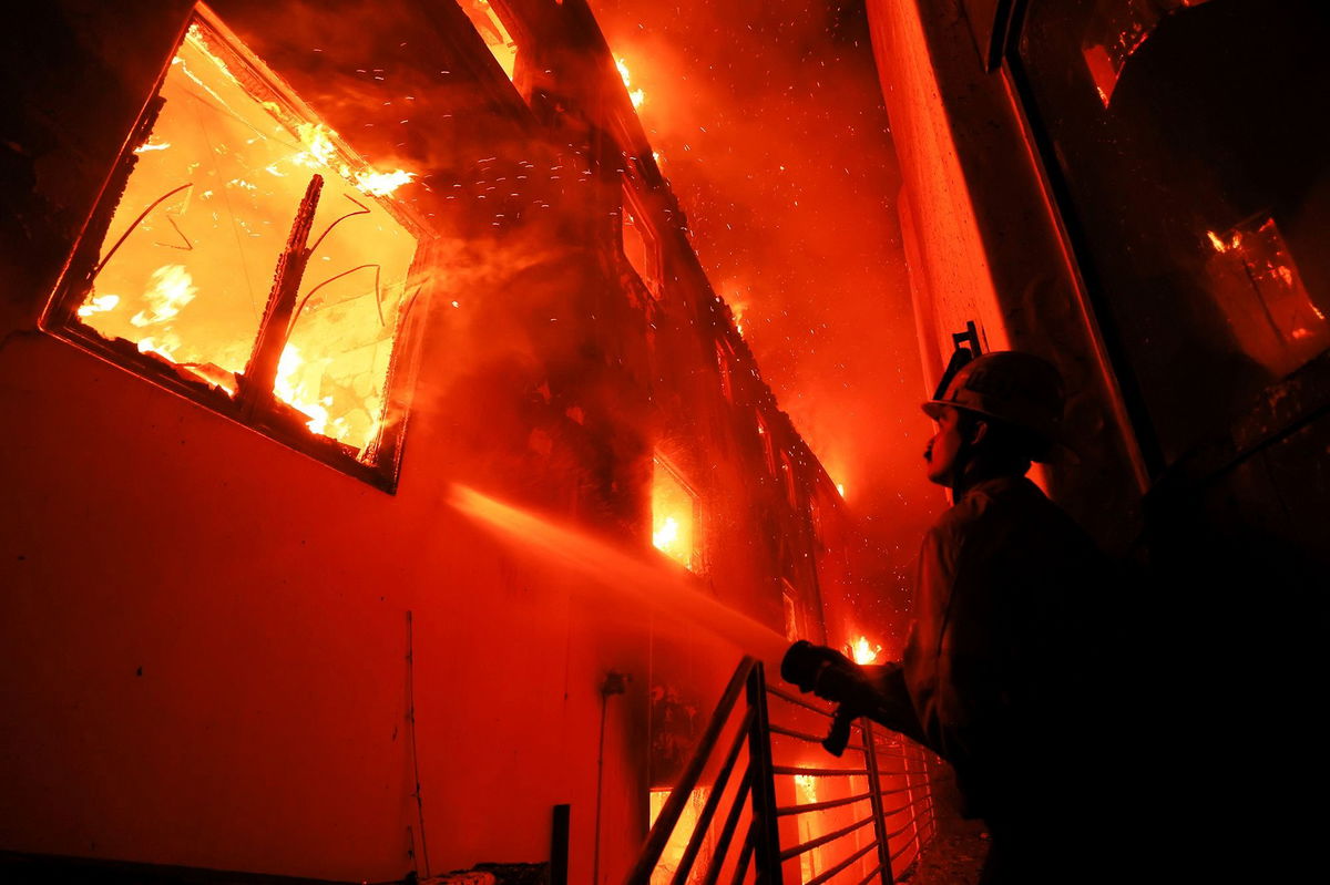 <i>Etienne Laurent/AP via CNN Newsource</i><br/>A firefighter works from a deck as the Palisades Fire burns a beach front property in Malibu on January 8.