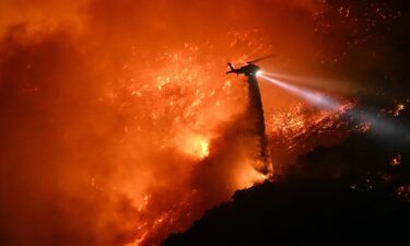 A fire fighting helicopter drops water as the Palisades fire grows near the Mandeville Canyon neighborhood and Encino