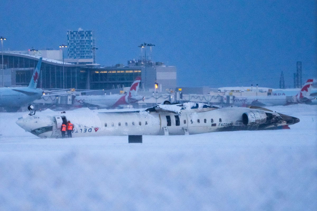 <i>Katherine KY Cheng/Getty Images via CNN Newsource</i><br/>Airport workers survey the site of a Delta Air Lines plane crash that injured at least 18 passengers at Toronto Pearson International Airport on February 18. None of the passengers or crew were killed in the crash.