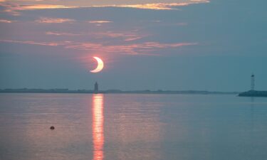 A partial solar eclipse is seen as the sun rises behind the Delaware Breakwater Lighthouse on June 10
