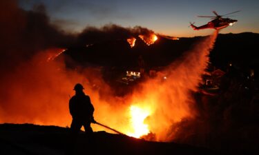 Fire personnel respond to homes destroyed while a helicopter drops water as the Palisades Fire burns on January 7.