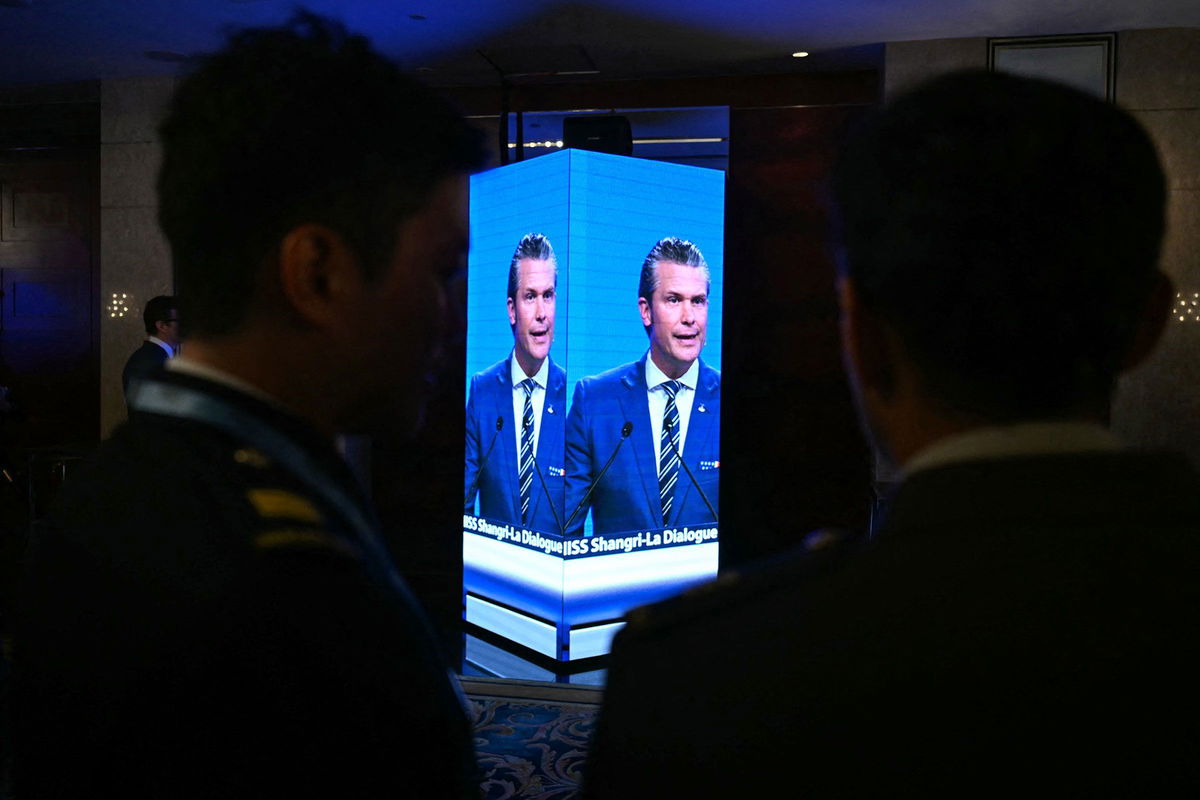 <i>Mohd Rasfan/AFP/Getty Images via CNN Newsource</i><br/>Attendees outside the ballroom watch on a screen as Secretary of Defense Pete Hegseth delivers an address at the Shangri-La Dialogue Summit in Singapore on Saturday
