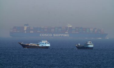 Two traditional dhows sail by a large container ship in the Strait of Hormuz Friday