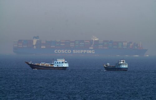 Two traditional dhows sail by a large container ship in the Strait of Hormuz Friday