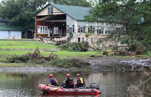 A search and rescue team floats Monday along the Guadalupe River past a damaged building at Camp Mystic in Hunt