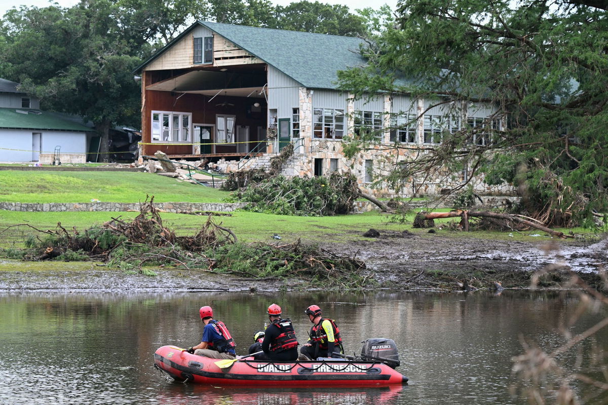 <i>Ronaldo Schemidt/AFP via Getty Images via CNN Newsource</i><br/>A search and rescue team floats Monday along the Guadalupe River past a damaged building at Camp Mystic in Hunt