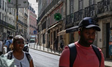 Pedestrians walk past a pharmacy sign showing 39 degrees celsius (86 Fahreneheit) as high temperatures hit Lisbon