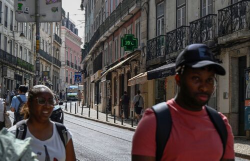 Pedestrians walk past a pharmacy sign showing 39 degrees celsius (86 Fahreneheit) as high temperatures hit Lisbon