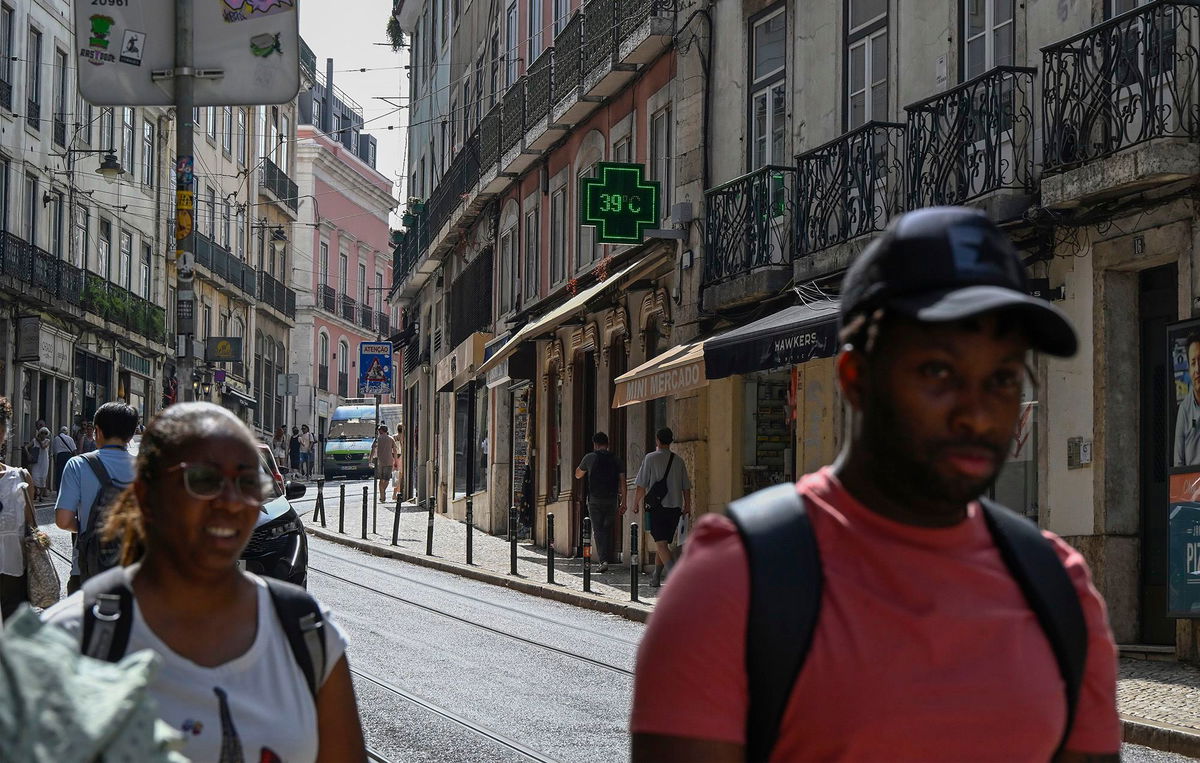 <i>Horacio Villalobos/Corbis News/Getty Images via CNN Newsource</i><br/>Pedestrians walk past a pharmacy sign showing 39 degrees celsius (86 Fahreneheit) as high temperatures hit Lisbon