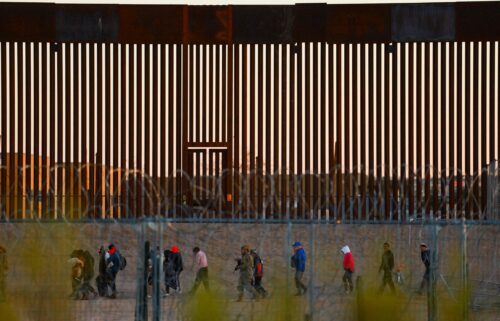 Migrants seeking asylum in the United States gather near the border wall after crossing a razor wire fence as a member of the Texas National Guard escorts them in December 2024.
