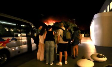 Tourists evacuate a hotel on Crete as wildfires burn.