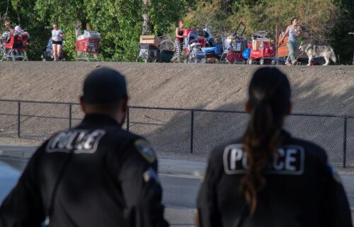 Stockton Police officers watch as inhabitants of a homeless encampment on an island on White Slough move their possessions onto a levee along Trinity Parkway near McAuliffe Road in north Stockton